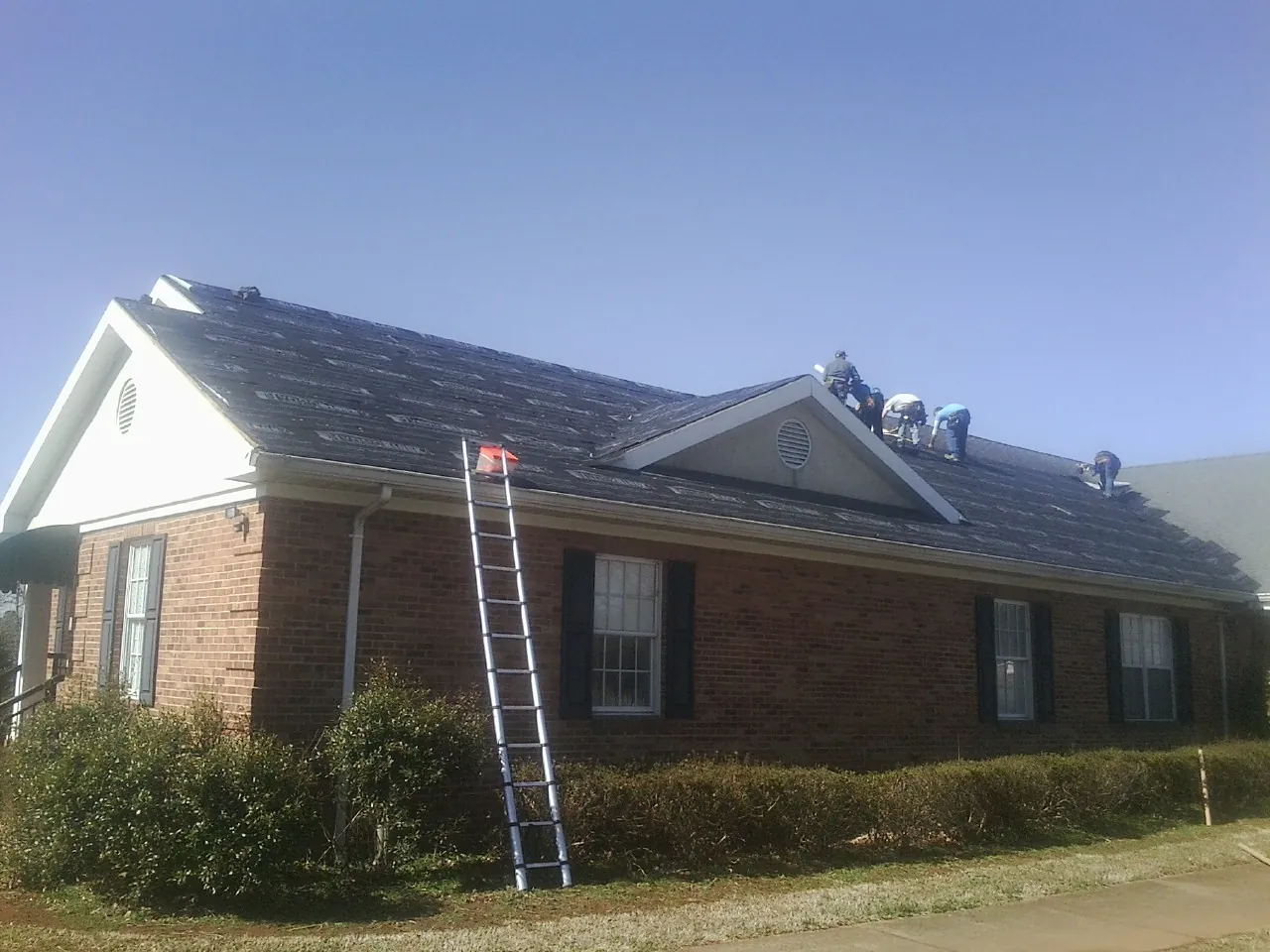 Crew tearing shingles off a brick ranch roof with a ladder set — Metal Roof Repair work by our crew in Grover