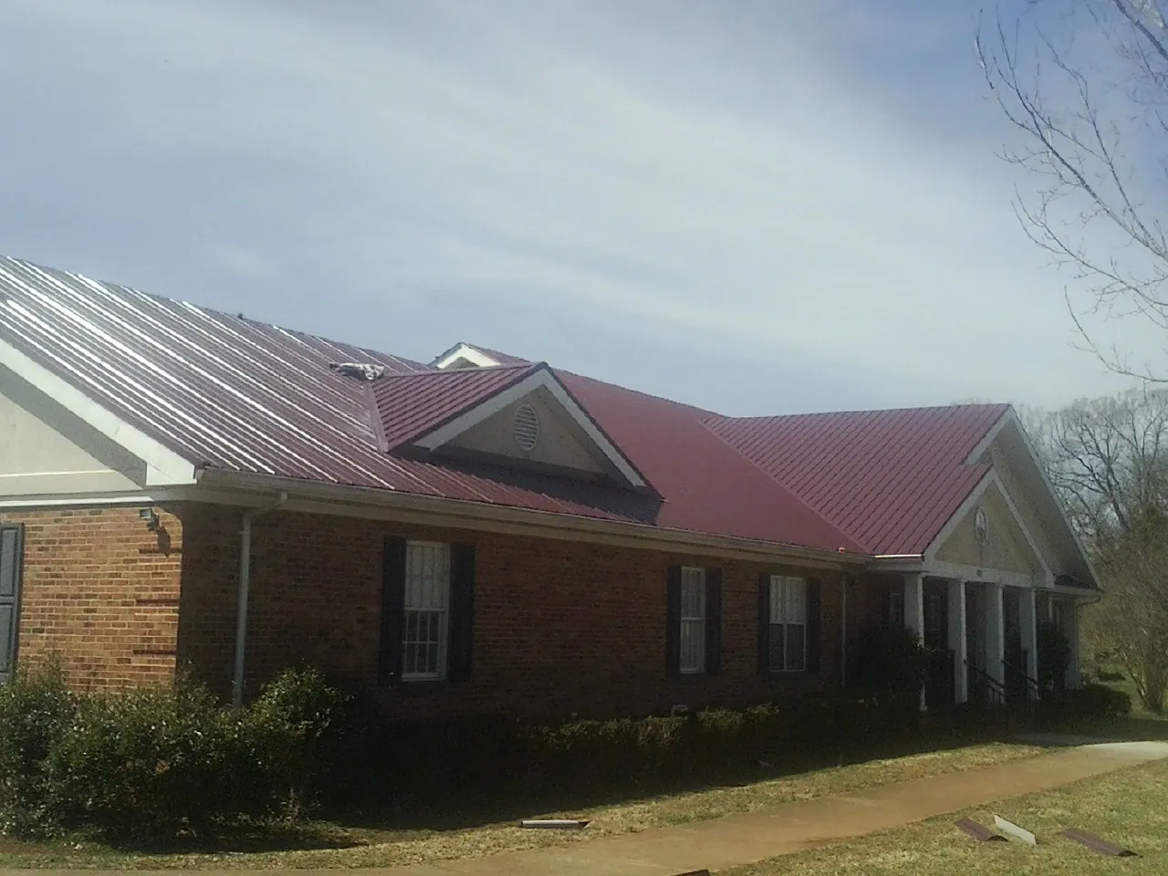 Red metal roof with gabled entries on a long brick building, from a Hail Damage Roof Repair job in Grover
