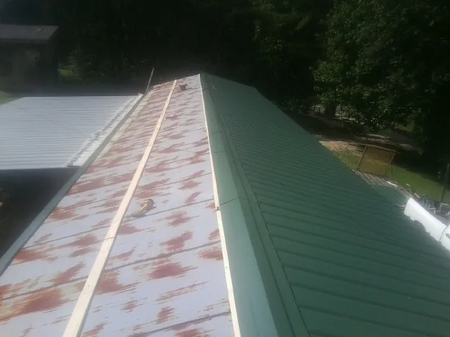 Old rusted panels beside newly installed green metal roofing — Wind Damage Roof Repair by Roofing Brothers in Grover
